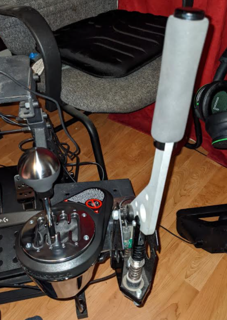 Thrustmaster TH8A Add-on shifter mounted at an angle next to a handbrake on a wheel stand